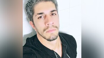 Primer plano de Pedram Azad, un hombre con cabello gris, barba y bigote, vistiendo una camisa negra, mirando directamente a la cámara