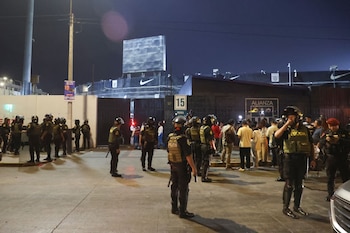 Vista nocturna de oficiales de policía con equipo antidisturbios frente a la entrada del Estadio Matute, con una multitud de personas en el fondo