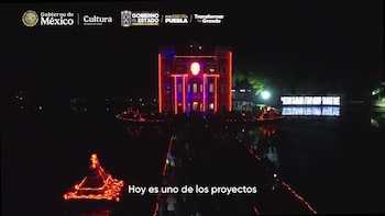 Edificio de noche adornado con luces rojas y una calavera brillante en la fachada, junto a un cuerpo de agua con reflejos