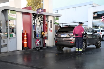 Un empleado de gasolinera con chaqueta rosa y gorra está repostando un SUV Jeep Compass gris en un surtidor con señales de Castrol y Quantum