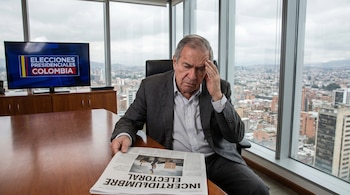 Hombre de traje sentado en oficina moderna, lee periódico. Pantalla de TV muestra 'Elecciones Presidenciales Colombia'. Ventanas con vista a una ciudad. Mano en la frente.