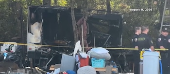 Los restos quemados de una casa rodante permanecen acordonados con cinta amarilla junto a tres oficiales de policía