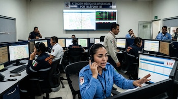 Centro de Atención Médica de Urgencias 137 con operadores en cubículos, usando auriculares y computadoras. Una mujer en primer plano habla. Pantalla grande con mapas.