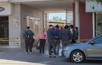 Grupo de personas, incluyendo familiares, de pie frente a la entrada de un edificio con cinta policial amarilla. Un coche gris está en primer plano