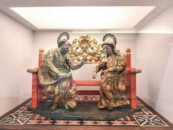 Dos estatuas de madera policromada y dorada sentadas en un banco decorado dentro de una vitrina de vidrio