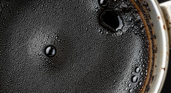 Primer plano de superficie oscura con burbujas, algunas grandes. Borde de recipiente metálico con residuos secos y oscuros.