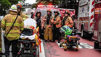 Grupo de bomberos y personal de emergencias con uniformes y cascos, dos camillas de rescate y dos vehículos de emergencia en una calle