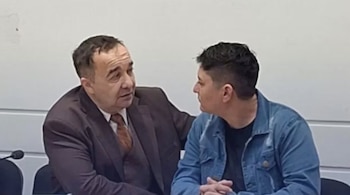Dos hombres sentados en un tribunal. El hombre mayor, de traje oscuro, abraza al joven, que viste chaqueta vaquera y camiseta negra. Se miran