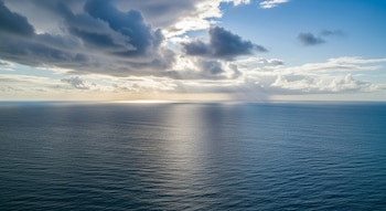 Vista aérea del océano Atlántico con su superficie azul, cielo con nubes oscuras y claras, y rayos de sol que se proyectan sobre el agua.