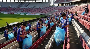 Aficionados japoneses en un estadio de futbol recogen residuos de las gradas en bolsas azules.