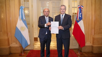 Dos hombres con traje y corbata, Pablo Quirno y el embajador de Chile, sostienen un documento oficial entre las banderas de Argentina y Chile