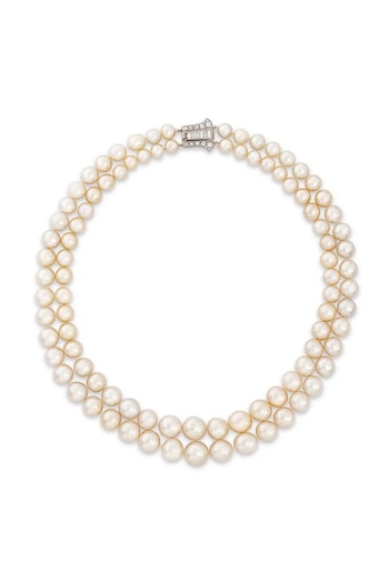 Un collar de perlas de doble hilera con perlas cremosas y un broche rectangular plateado con diamantes, sobre un fondo blanco liso