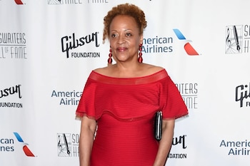 Cassandra Wilson luce un vestido rojo y pendientes a juego frente a un panel blanco con varios logotipos