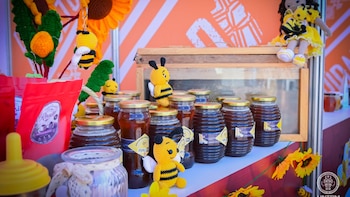 Frascos de miel, abejas de tejido, girasoles de tejido, una muñeca de tejido con una abeja y bolsas rojas en una exhibición