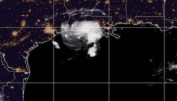 Vista satelital nocturna de una masa de nubes blancas sobre la línea costera delimitada por puntos luminosos dorados