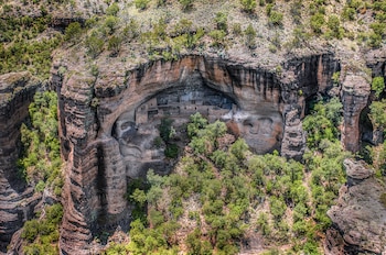Vista aérea de las ruinas de Cuarenta Casas, estructuras de adobe integradas en una cueva natural en un acantilado rocoso cubierto de vegetación verde