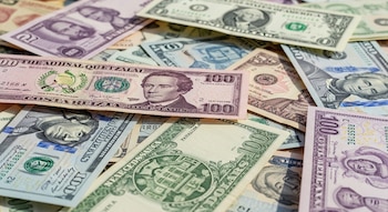 Un conjunto de billetes de quetzales, dólares estadounidenses, colones, balboas y pesos dominicanos de distintas denominaciones se presenta apilado sobre una superficie.