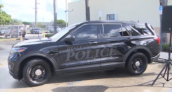Un vehículo policial negro con el rótulo de la Policía de Hialeah estacionado en un área exterior junto a un altavoz montado sobre un trípode