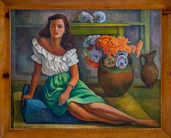 Pintura al óleo que muestra a una mujer sentada en un sofá azul, con blusa blanca y falda verde, junto a un jarrón de barro con flores de varios colores y un cántaro