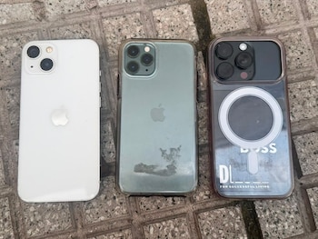 Tres teléfonos móviles iPhone: uno blanco, uno verde con funda transparente y uno oscuro con funda transparente y un aro MagSafe