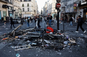 Unas personas pasan junto a los restos de una hoguera callejera tras los enfrentamientos entre la policía antidisturbios y los manifestantes en París, Francia, el 18 de octubre de 2026. EFE/EPA/MOHAMMED BADRA