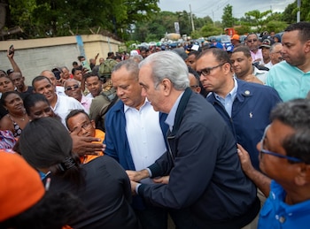 El presidente Luis Abinader, de camisa clara y chaqueta, camina con un grupo. Un hombre de azul señala adelante. Están en un paso elevado con barandales naranja y verde