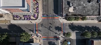 Vista aérea de una intersección urbana con cuatro cruces peatonales de colores arcoíris, flanqueadas por edificios y aceras con mesas al aire libre
