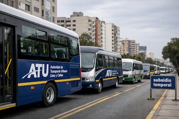 Vista lateral de una larga fila de autobuses modernos de la ATU estacionados en una avenida de Lima bajo un cielo nublado, con edificios al fondo y un cartel de 'subsidio temporal'.