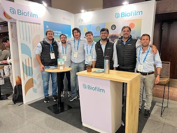 Seis hombres posan frente a un stand de exposición con el logo Biofilm, mesas pequeñas y un cartel que indica 'TODO TRIGO 2023'