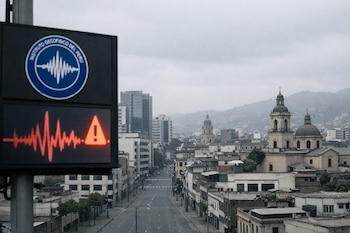 Una pantalla electrónica con el logo del IGP y una alerta sísmica roja con sismograma y exclamación, con una ciudad peruana de edificios y calles vacías al fondo bajo cielo gris.