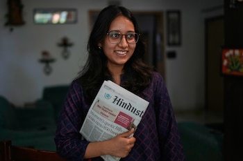 Primer plano de una joven india con gafas y cabello oscuro, sonriendo mientras sostiene el periódico Hindustan Times en sus manos