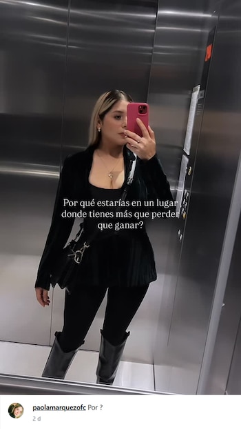 Paola Márquez se toma una selfie en un ascensor con un teléfono rosado. Viste chaqueta oscura, top, pantalones y botas negras, con texto superpuesto