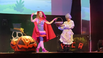 Dos personas disfrazadas representan una obra en un escenario decorado con una gran calabaza y una canasta