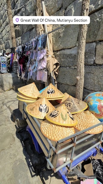 Primer plano de un puesto de souvenirs con sombreros cónicos de paja, varios con dibujos de pandas y hojas, y un gran globo terráqueo azul al fondo, junto a una pared de piedra
