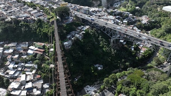 Fotografía aérea de un puente metálico con vehículos, un puente ferroviario y casas construidas en la ladera de un barranco