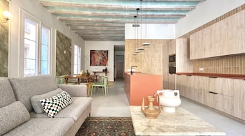 Interior de un apartamento moderno con sala, comedor y cocina de concepto abierto, con sofá gris, mesa de madera, cocina color salmón y vigas en el techo.