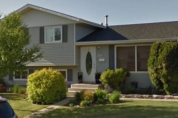 Una casa residencial gris de dos pisos con techo oscuro, puerta blanca con vidrio ovalado y el número 304 visible. Hay arbustos y un camino de entrada