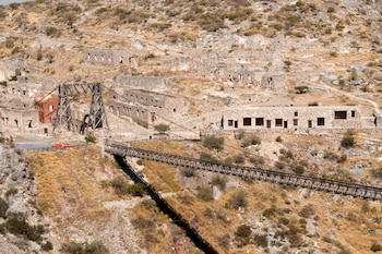 Vista aérea del Puente de Ojuela, un puente colgante largo, y las ruinas de numerosos edificios de piedra. El terreno es árido con vegetación seca
