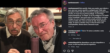 Dos hombres mayores sentados, uno con bigote y gafas redondas mirando al frente, el otro sonriendo levemente con gafas rectangulares y bufanda