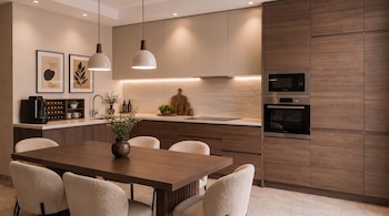 Una cocina moderna con mesa de comedor de madera, cinco sillas tapizadas, gabinetes, horno, microondas, fregadero, cafetera, plantas, cuadros y luces.