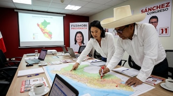 Keiko Fujimori y Roberto Sánchez, en camisa blanca, analizan un mapa grande de Perú sobre una mesa, señalando regiones. Un proyector muestra datos electorales.