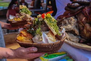 Manos sostienen una canasta de mimbre con Chiriuchu, un plato peruano frío con carne oscura, tortilla frita, algas, queso, pimientos rojo y amarillo