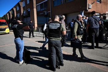Agentes con chalecos de la Policía Judicial y personas reunidas frente a un edificio escolar junto a un vehículo de emergencias