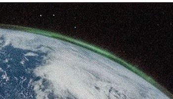Vista de la curvatura terrestre con masas de nubes y una fina capa verde brillante en el horizonte sobre el fondo del espacio