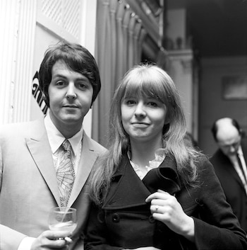 Fotografía en blanco y negro de Paul McCartney con traje sosteniendo una copa junto a Jane Asher con abrigo