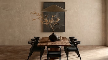 Comedor moderno con mesa de madera rectangular, seis sillas negras, jarrón oscuro con ramas amarillas, arte abstracto en pared beige y lámpara colgante de mimbre.