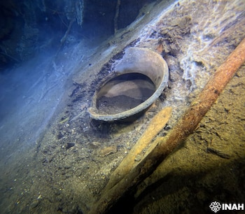 Fragmento de vasija o canaleta de cerámica, junto a dos objetos alargados sumergidos, en un lecho marino con arena y sedimentos