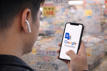 Vista trasera de una persona en una tienda de Japón con un AirPod en la oreja, sosteniendo un teléfono con el logo de Google Translate en la pantalla.