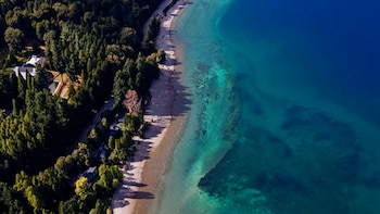 Vista aérea de una playa de arena junto a un bosque arbolado y un mar de aguas turquesas y azules
