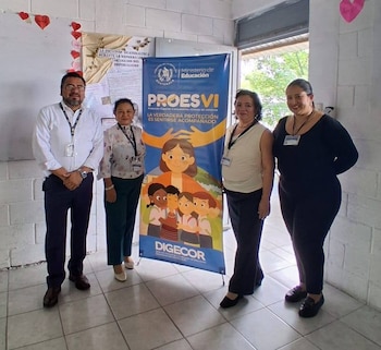 Cuatro adultos posan frente a un banner azul del programa PROESVI del Ministerio de Educación de Guatemala, mostrando niños y una figura adulta protectora